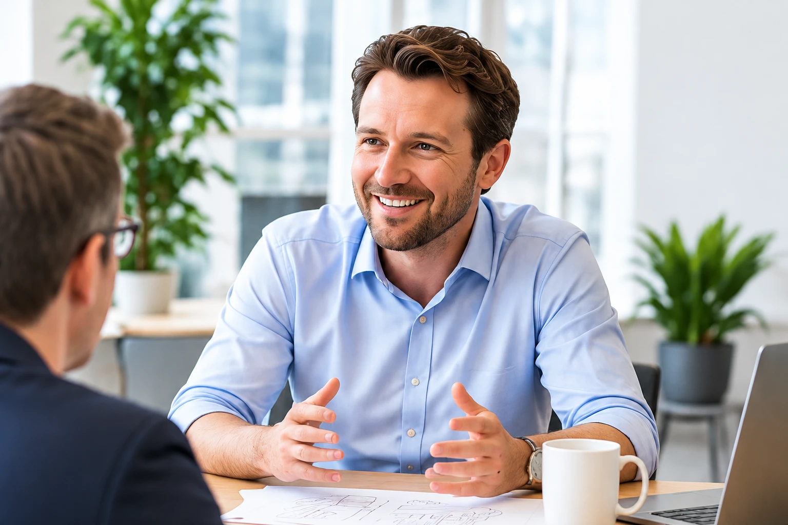 Adviseur in lichtblauw overhemd in gesprek aan een werktafel, met schets en koffiebeker erbij